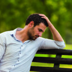 Depressed businessman is sitting at the park and thinking about